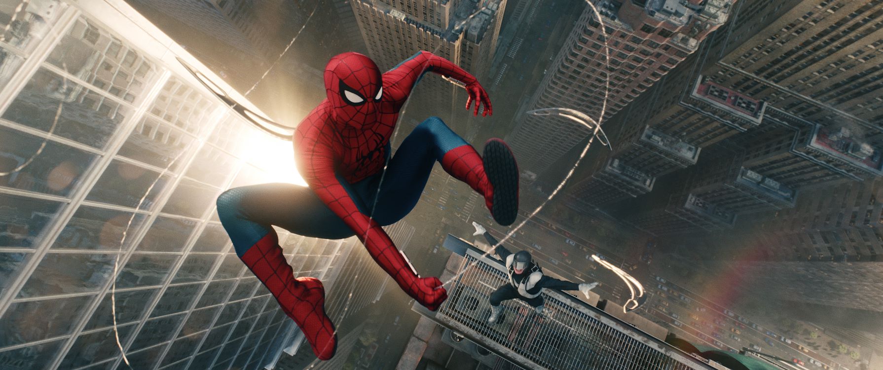 Spider-Man zwiert in zijn nieuwe rood-blauwe pak aan een web hoog boven de straten van New York, op een dak onder hem staat een figuur in een donker pak, officieel persbeeld uit Spider-Man: Brand New Day