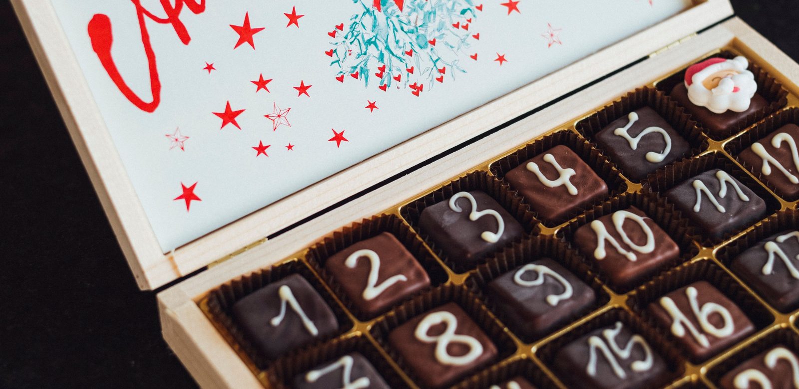 Een houten adventskalender met genummerde chocolaatjes en een kerstmannetje van suiker