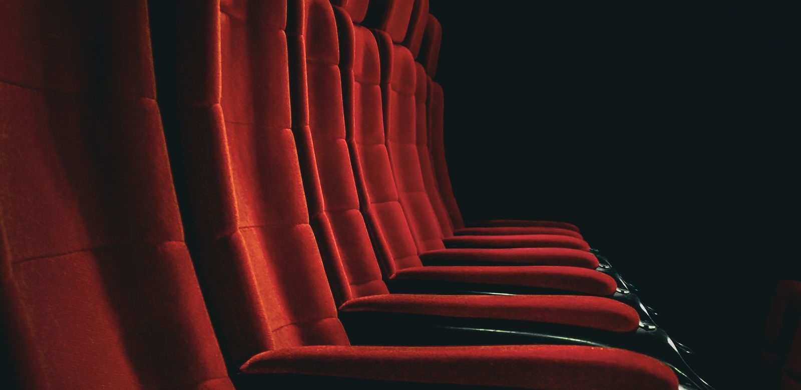 Een dramatisch zijaanzicht van lege rode fluwelen stoelen in een schemerige theaterzaal