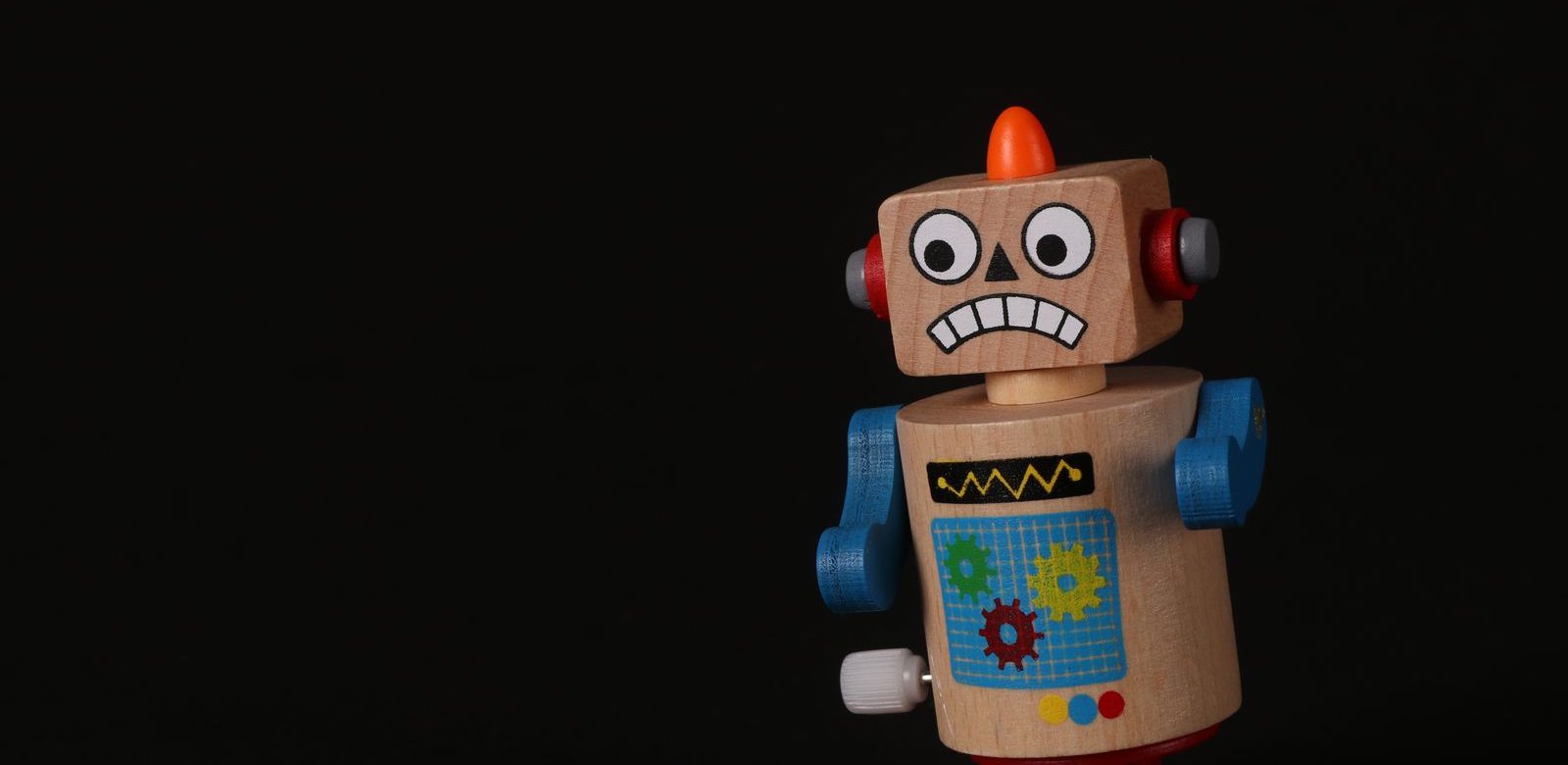 Een houten speelgoedrobot met opwindsleutel en een oranje kuif staat tegen een zwarte achtergrond