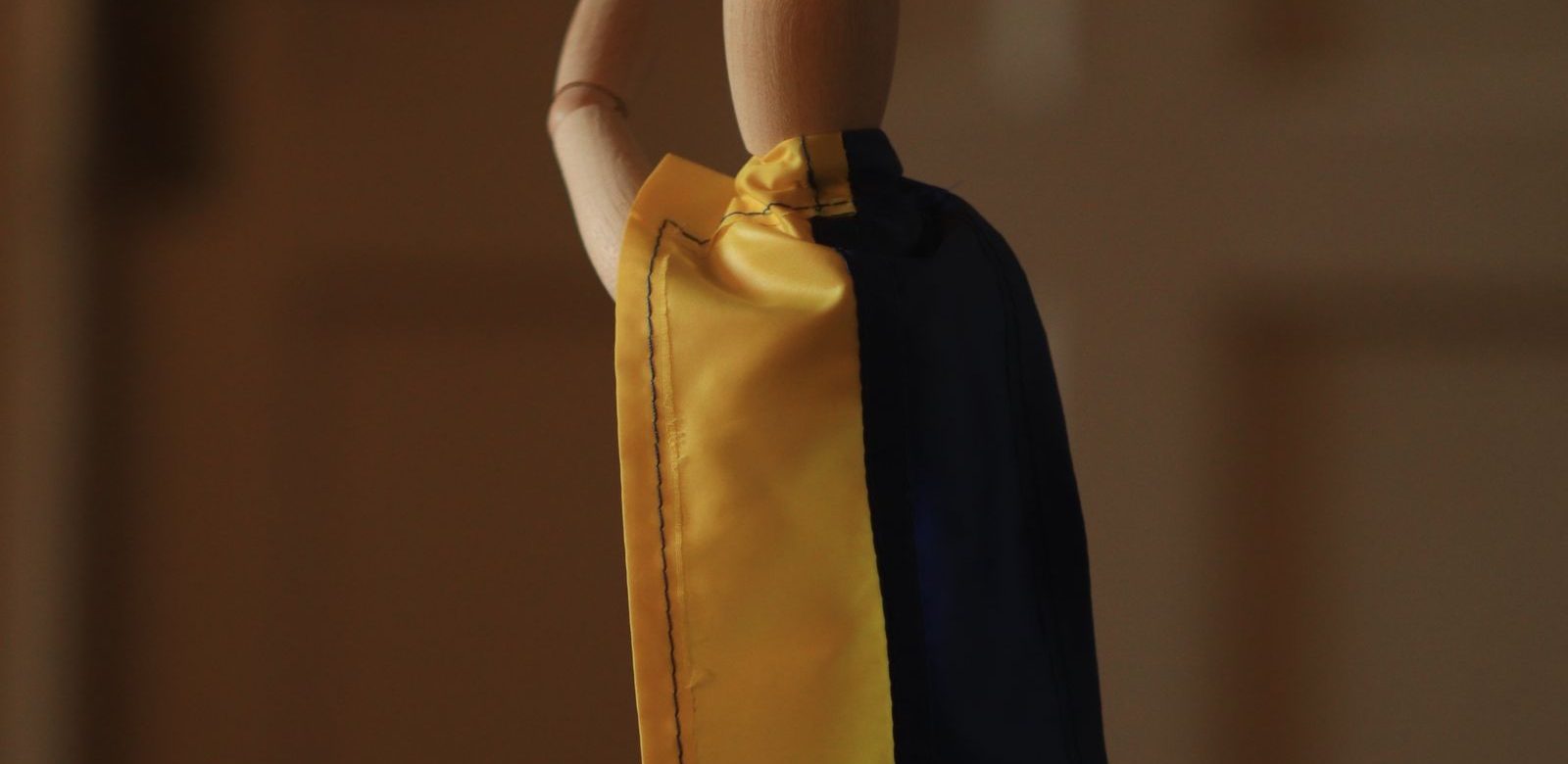 Houten pop met een gele en blauwe cape in een dramatische pose binnen