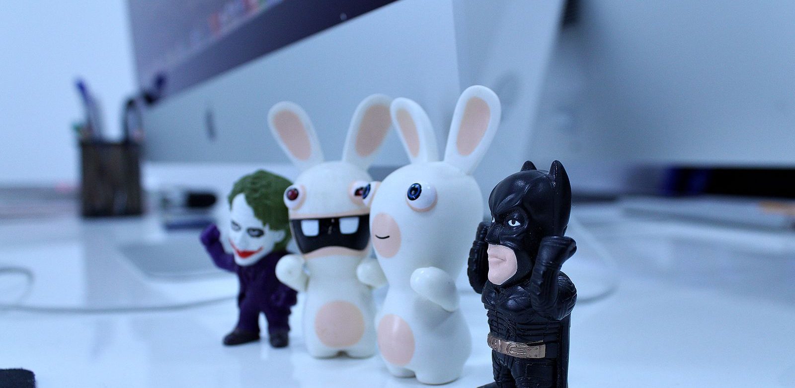 Kleine verzamelfiguurtjes op een bureau: de Joker, twee witte konijnen en Batman voor een computerscherm