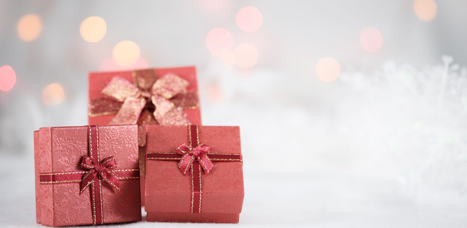 Drie rode cadeaudoosjes met strikken op een witte ondergrond, met wazige lichtjes op de achtergrond