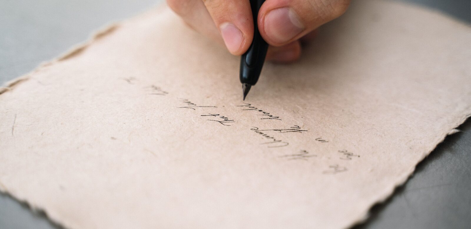 Een hand schrijft met een zwarte pen op een vel geschept papier