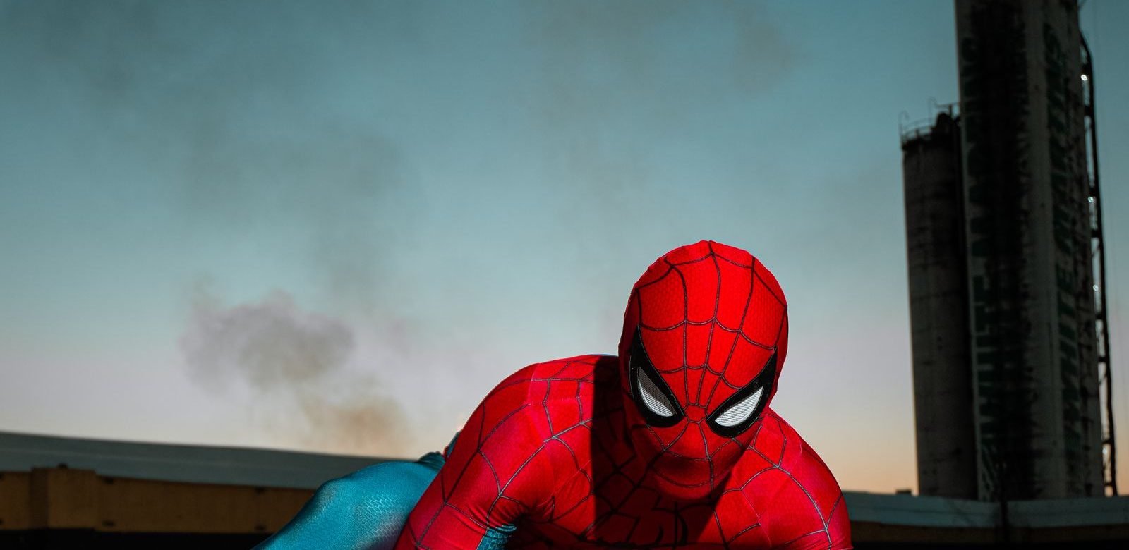 Iemand in een Spider-Man-pak hurkt op een dak bij zonsondergang