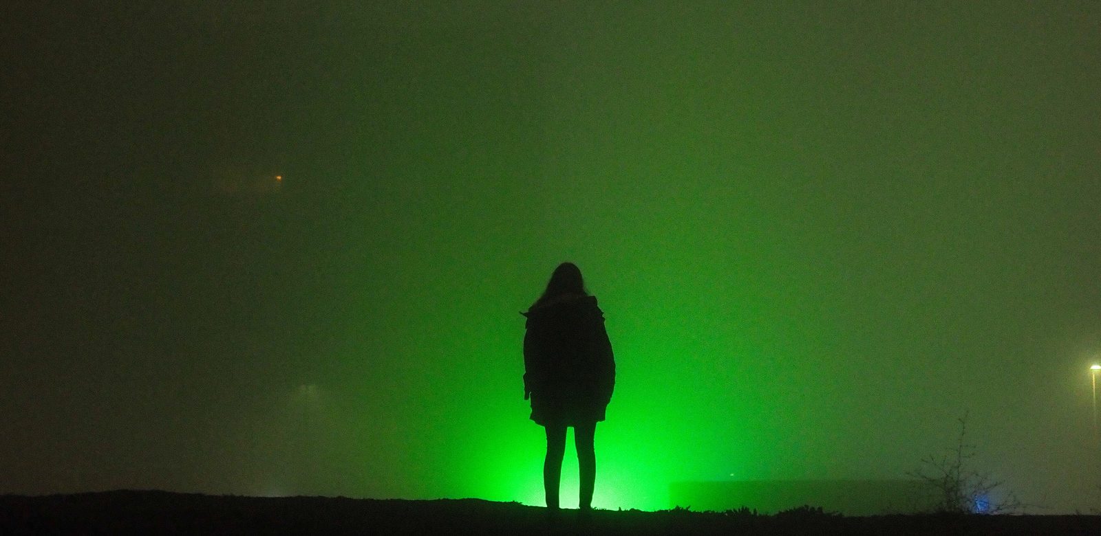 Een silhouet van een persoon in het donker, voor een fel groen licht in de mist