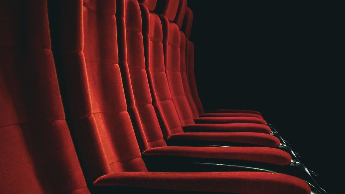 Lege rode fluwelen stoelen in een schemerige bioscoopzaal, van opzij gezien